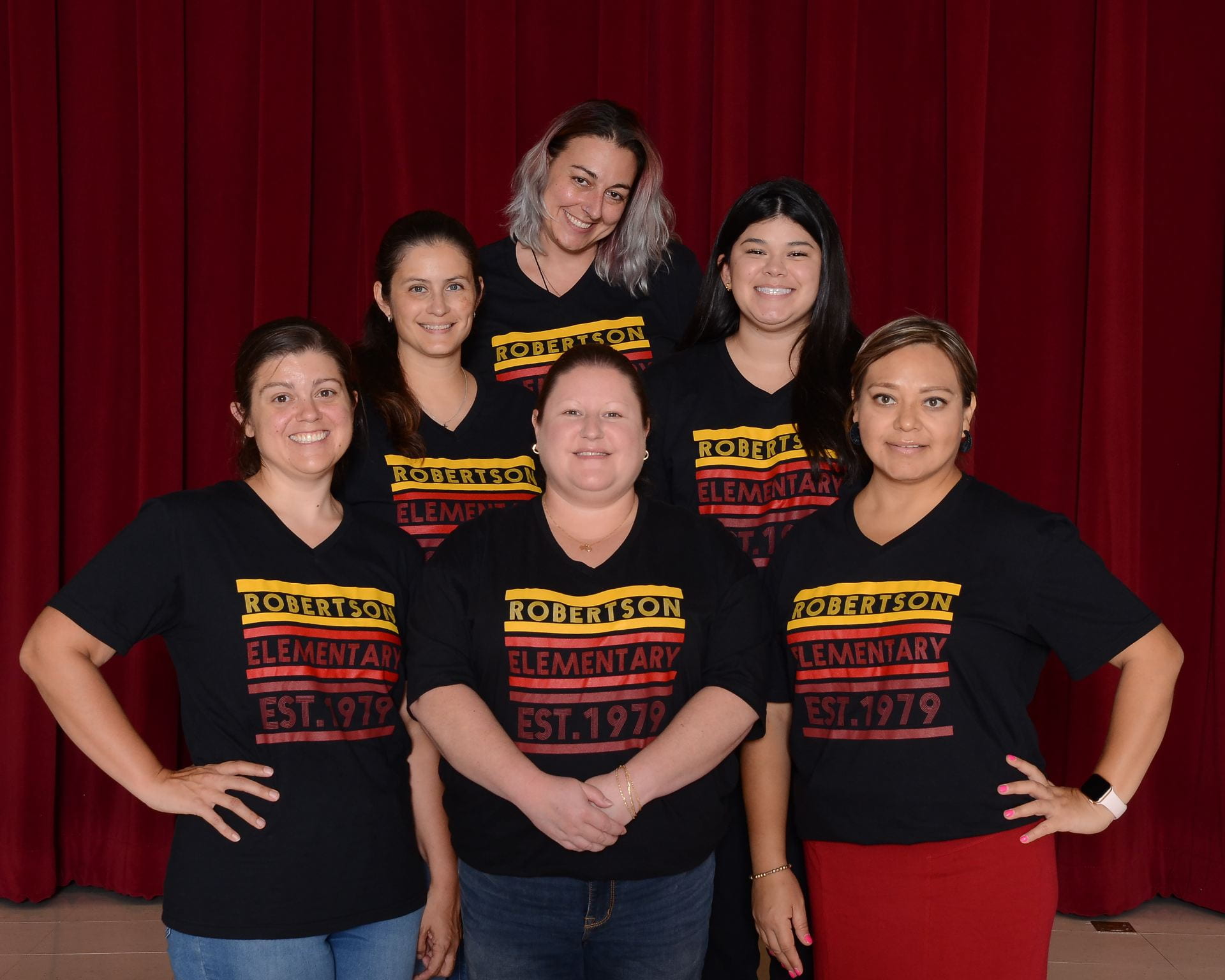 Six staff members wearing matching school shirts, stand in front of a dark background