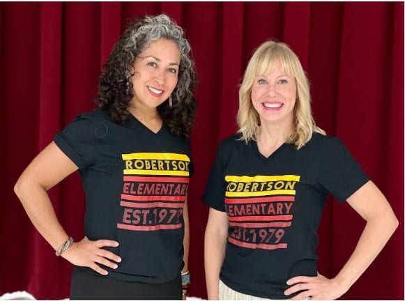 Two staff members wearing matching school shirts stand in front of a dark background