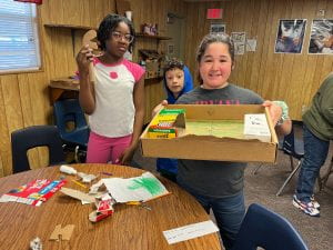 picture shows three fifth grade students presenting their cardboard creations